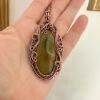 Artystyczny wisior z miedzi z pasami na kamieniu jako osobisty amulet na lancuszku.